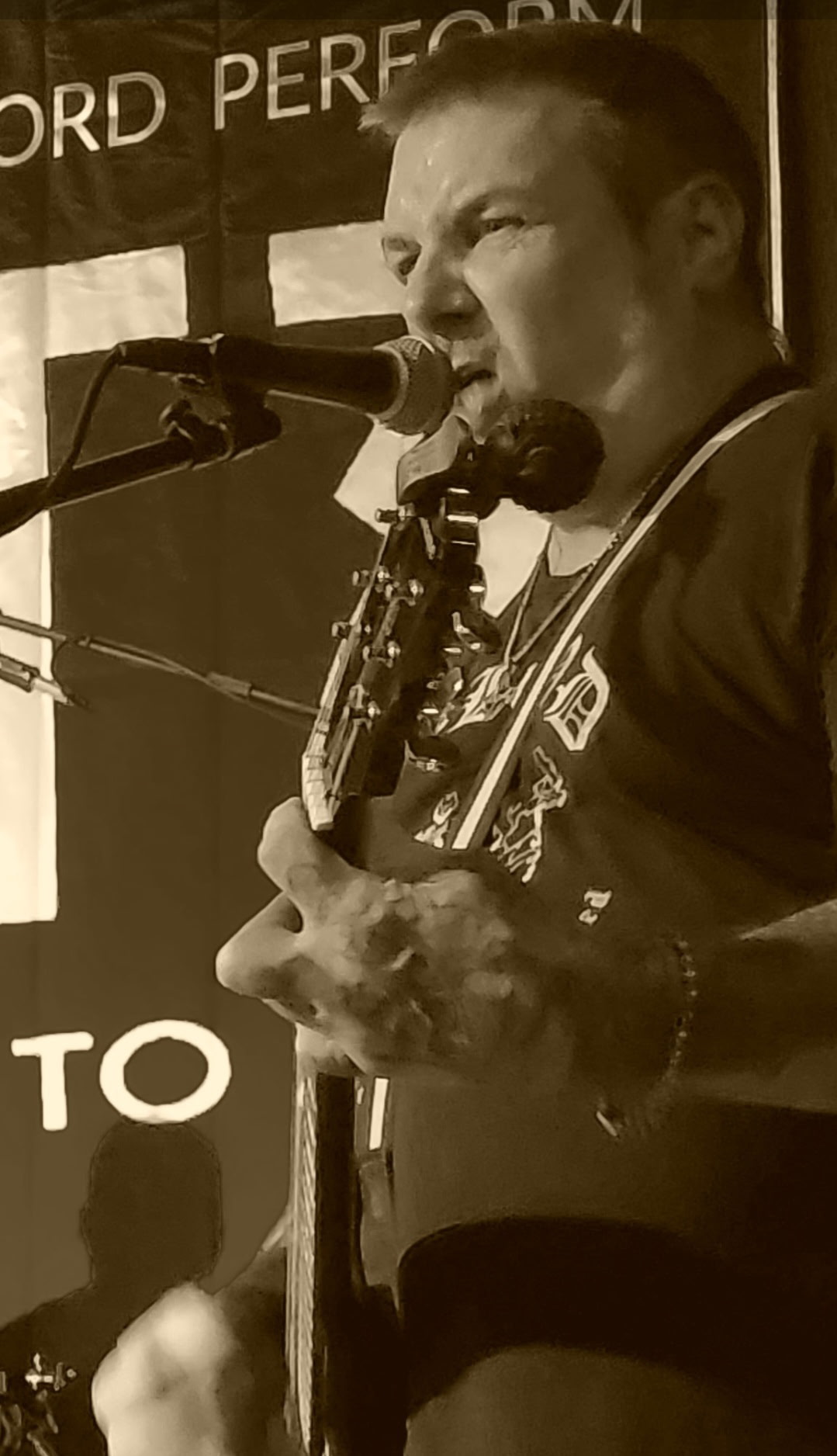 Sepia photo of a guitarist singing into a microphone on stage